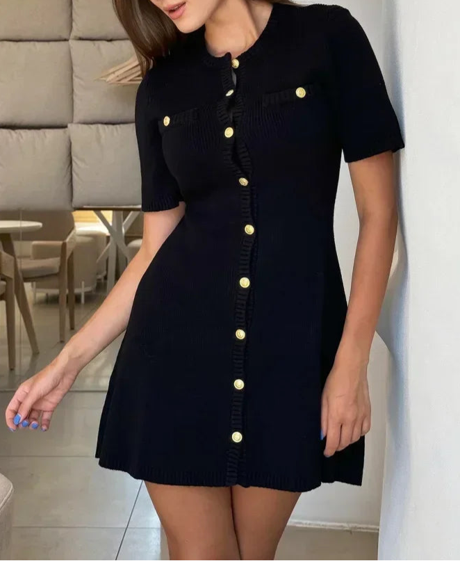 Woman wearing a black dress with gold buttons in an indoor setting