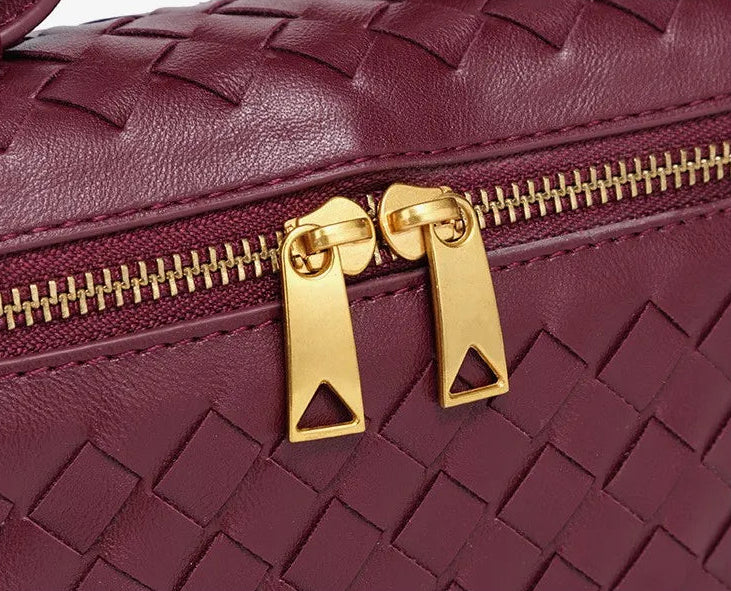 Maroon woven handbag with gold zipper on a white background