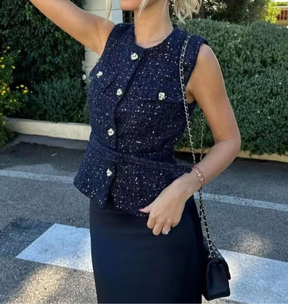 Woman in a navy blue peplum top and black skirt standing outdoors.