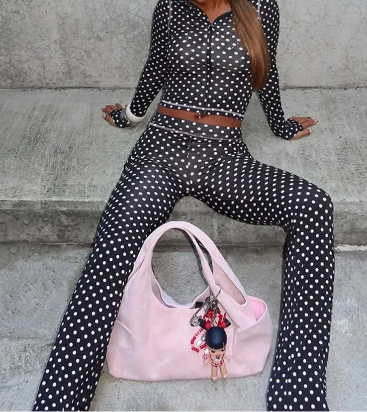 Person wearing a black polka dot outfit with a pink handbag on concrete steps.