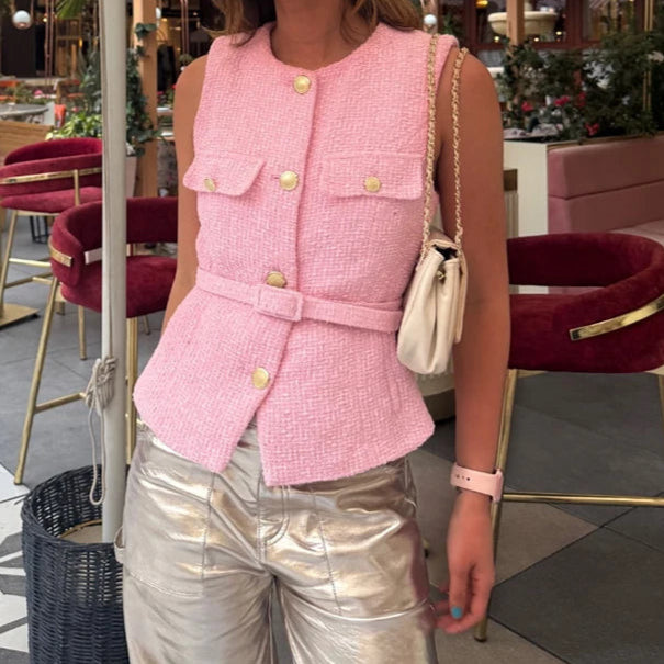 Woman wearing a pink sleeveless top with buttons in an outdoor setting.